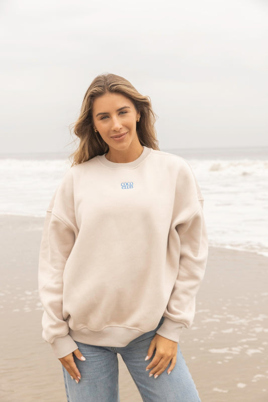 The Coco Club crewneck sweatshirt from House of Coco is made from premium cotton and polyester. It is beige/tan in color and features the "Coco Club" text embroidered on the front, and an inspiring message screen printed on the back of the sweatshirt which says "We rise by lifting others". this crewneck is a unisex oversized fit.